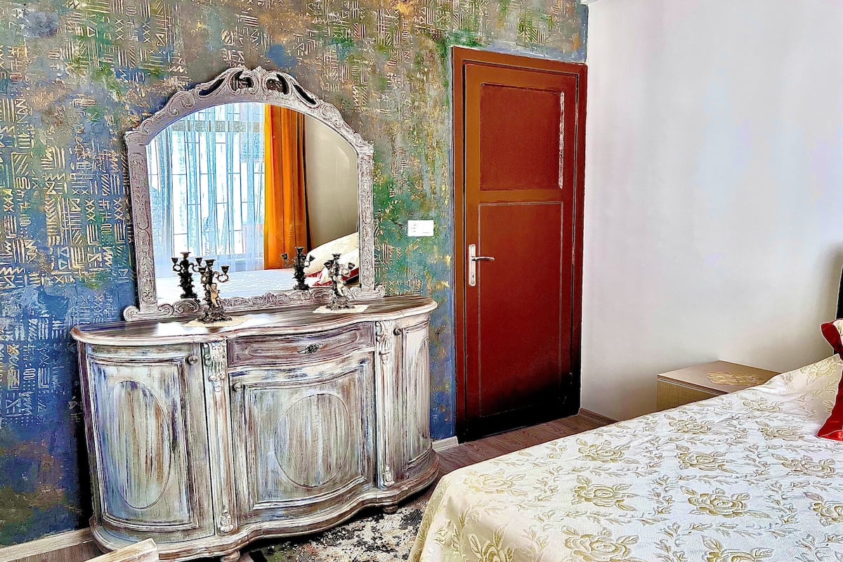 A room with a vintage-style dresser, a mirror, a red door, and a bed with a floral bedspread.