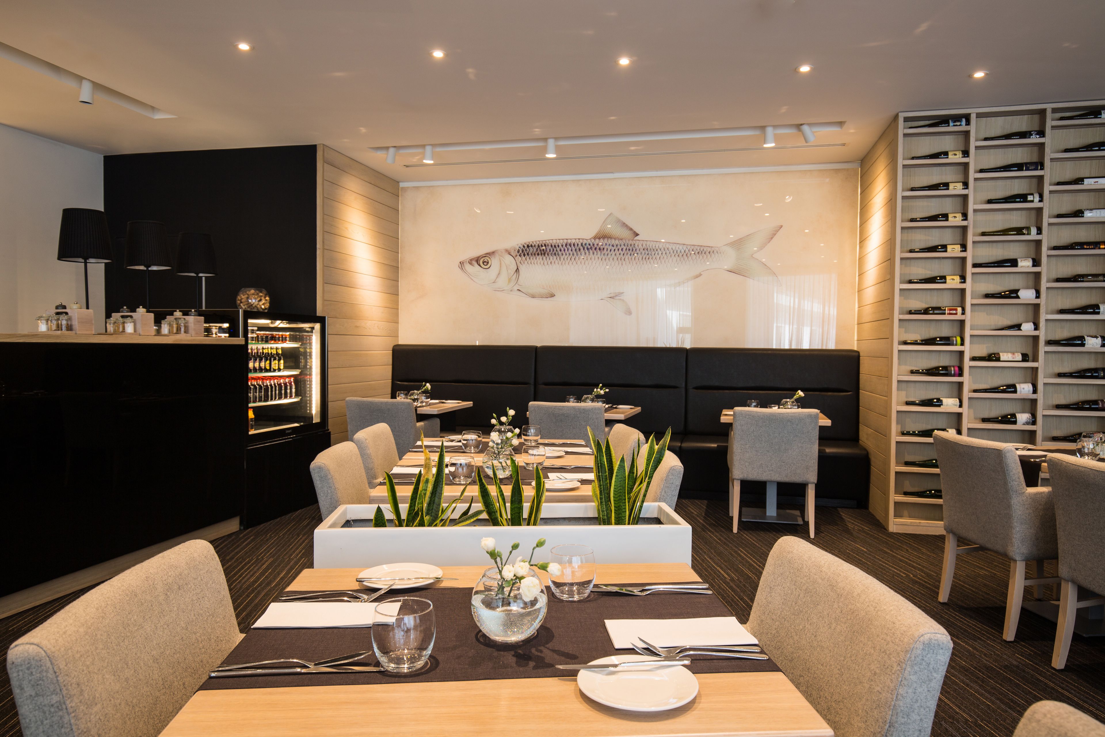 Un restaurant décoré d’une grande fresque représentant des poissons, doté d’un mobilier moderne et d’un présentoir à bouteilles de vin.