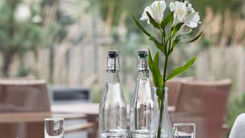 Mesa de comedor al aire libre con botellas de vidrio transparente, un florero con flores blancas y saleros y pimenteros.
