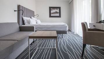 A modern hotel room with a grey sofa, a single bed, a small table, and a chair.