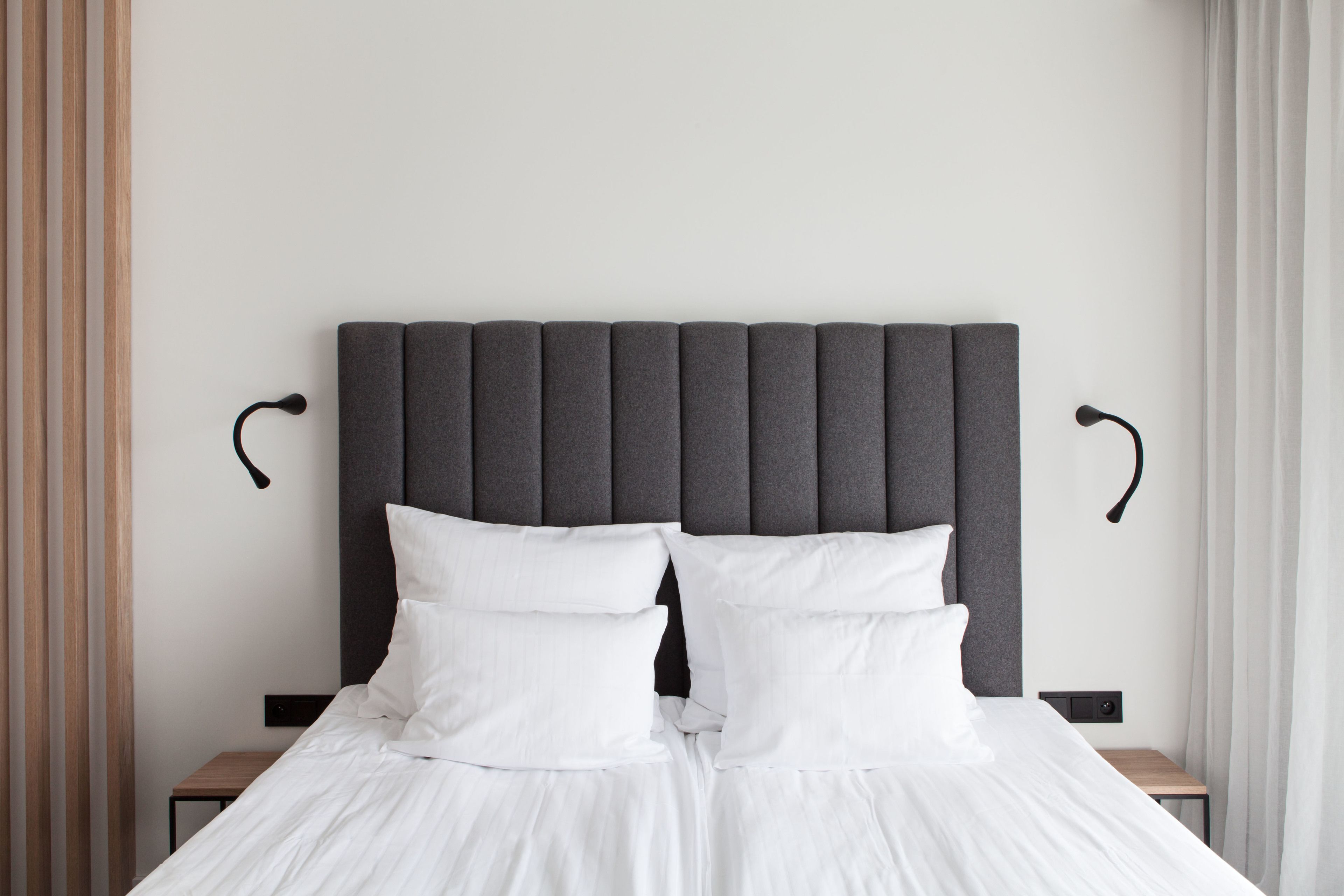 A neatly made bed with white linens and a dark headboard, flanked by two nightstands with black lamps.