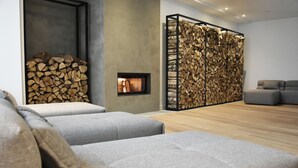 Un salon moderne avec des canapés gris, une cheminée et un mur décoré de bûches empilées.