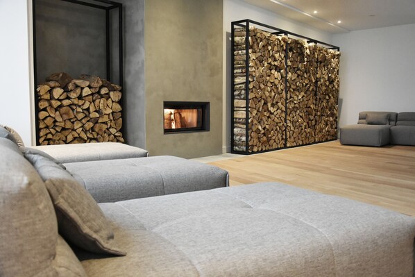 A modern living room with grey sofas, a fireplace, and a wall decorated with stacked logs.