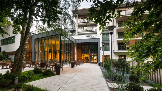 Un bâtiment moderne doté d’une façade en verre, d’un espace extérieur aménagé pour s’asseoir et d’un jardin bien entretenu.