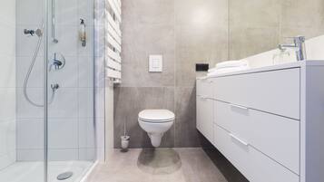 A modern bathroom with a glass-enclosed shower, a toilet, and a vanity with a mirror.