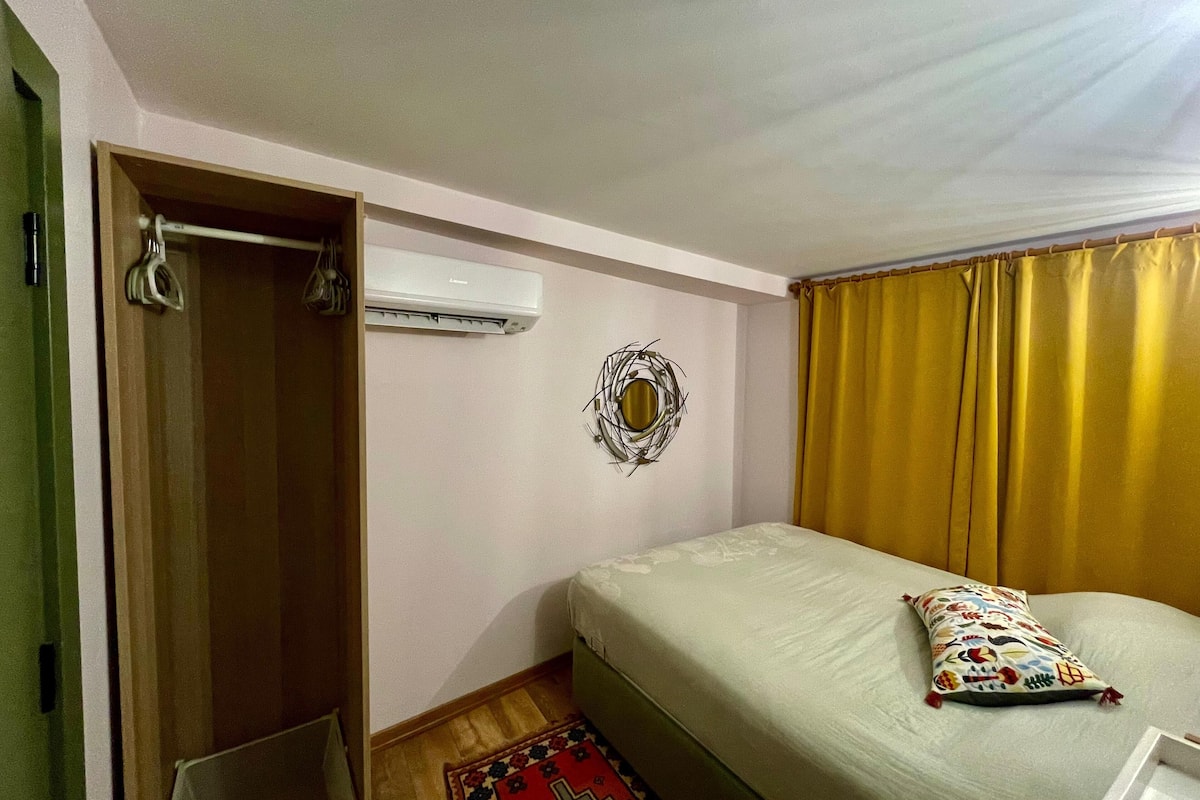 Habitación de hotel con cama, aire acondicionado instalado en la pared, espejo decorativo y ventana con cortinas.