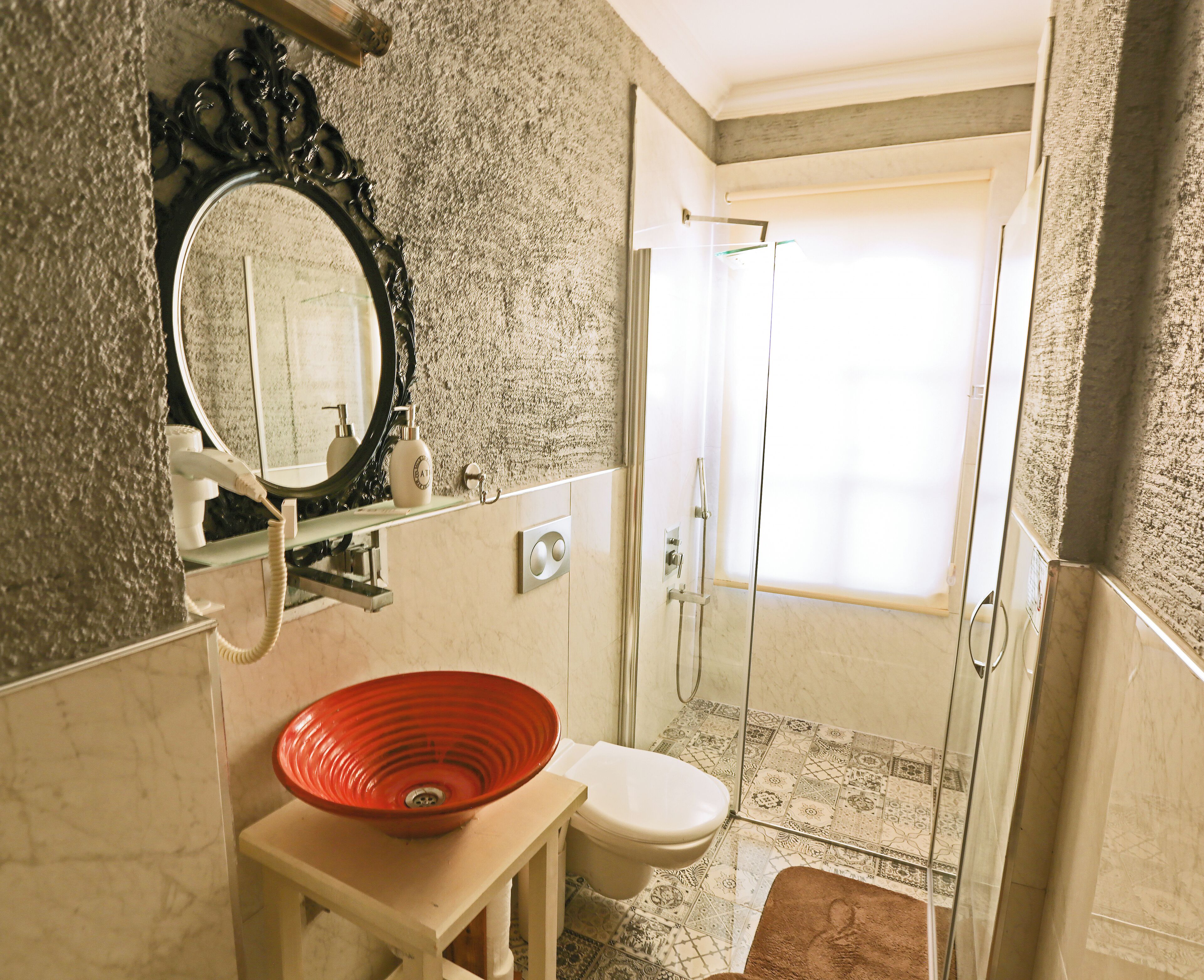 Un baño con pared de mármol, un lavamanos rojo, un inodoro y una zona de ducha.