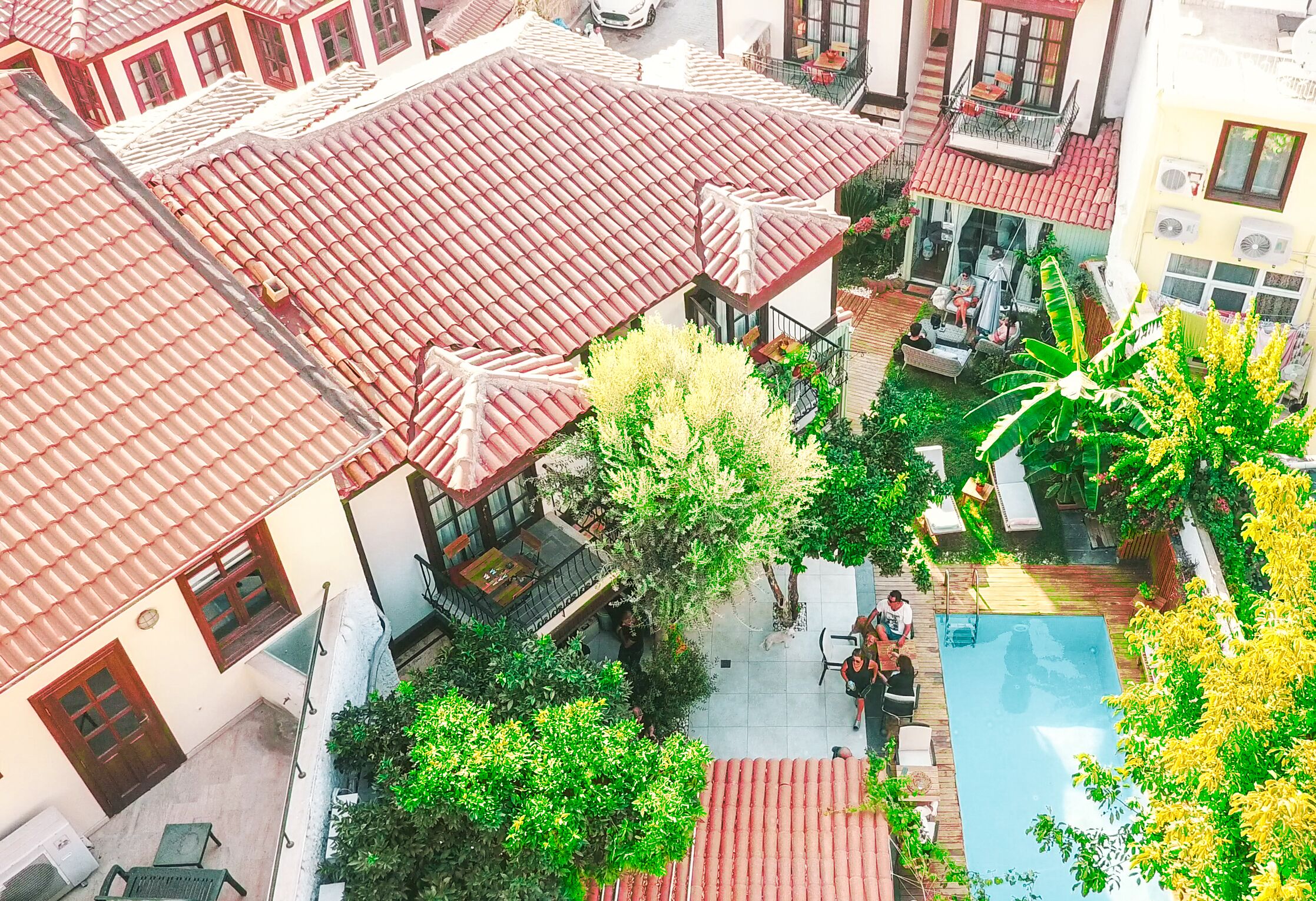 Vista aérea de un patio con piscina, techos de tejas rojas y zonas de estar al aire libre.