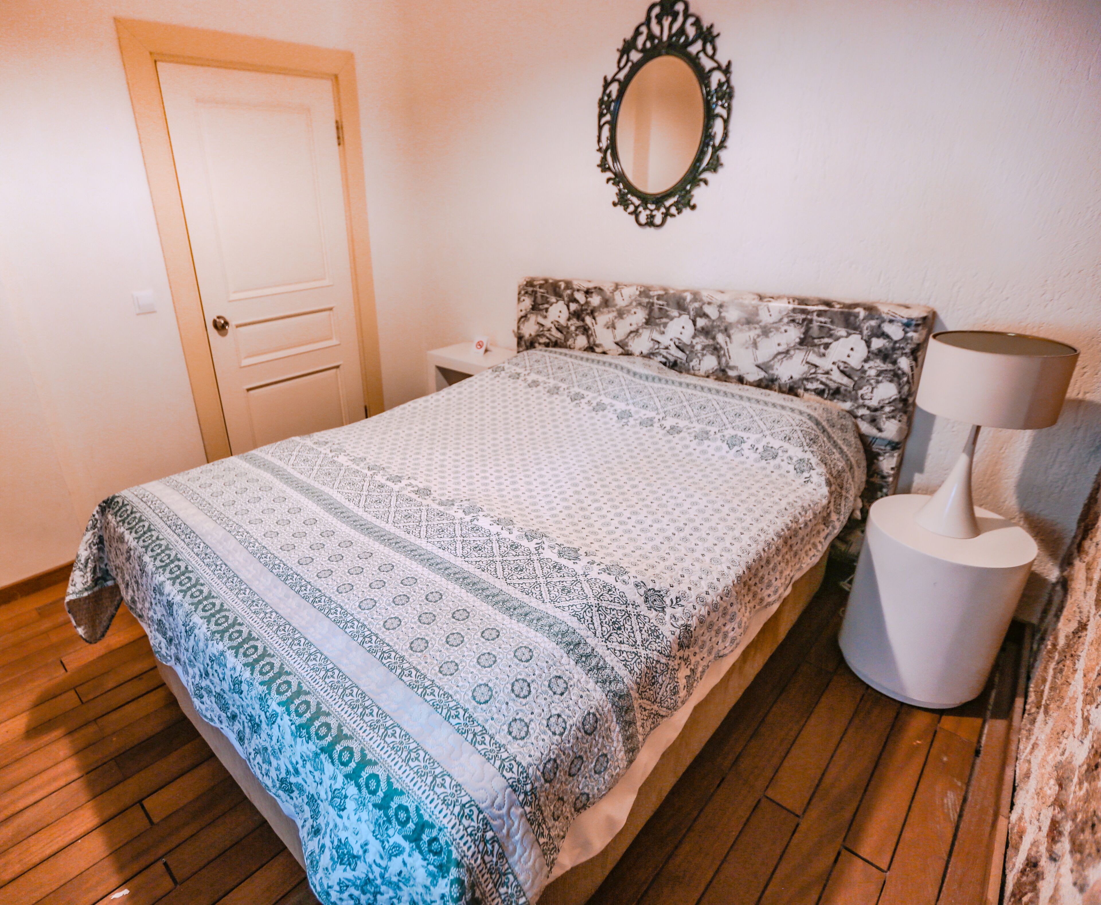 Une chambre à coucher avec un lit, une table de chevet, une lampe, un miroir et une porte.