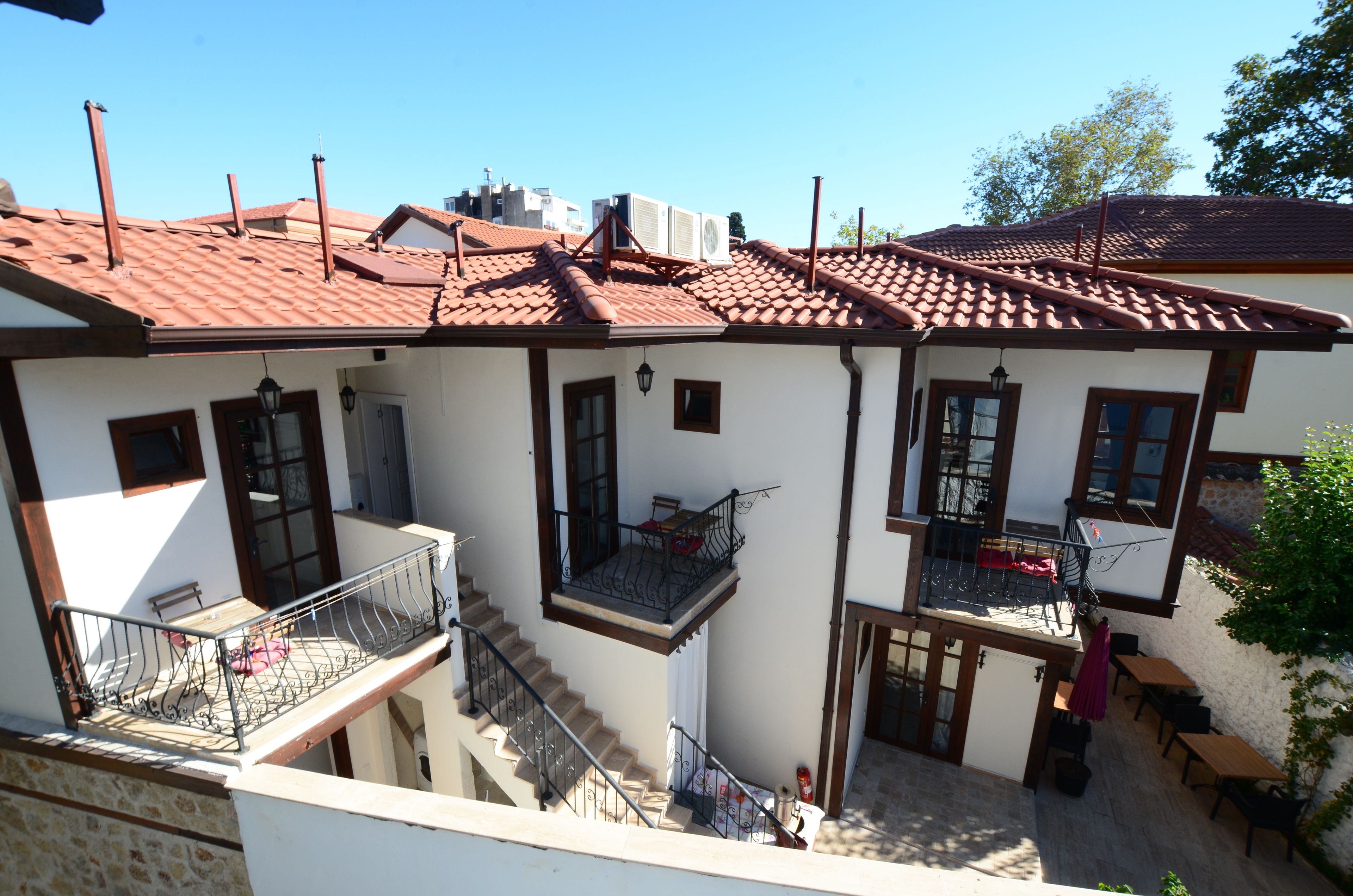 Un bâtiment à deux étages, doté d’un toit recouvert de tuiles rouges, de nombreux balcons et d’espaces aménagés pour s’asseoir à l’extérieur.