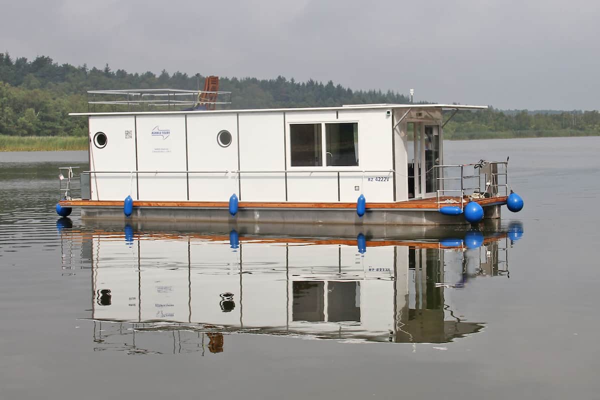 Ein feststehendes Hausboot mit Kabine, Fenstern und einem kleinen Deck.