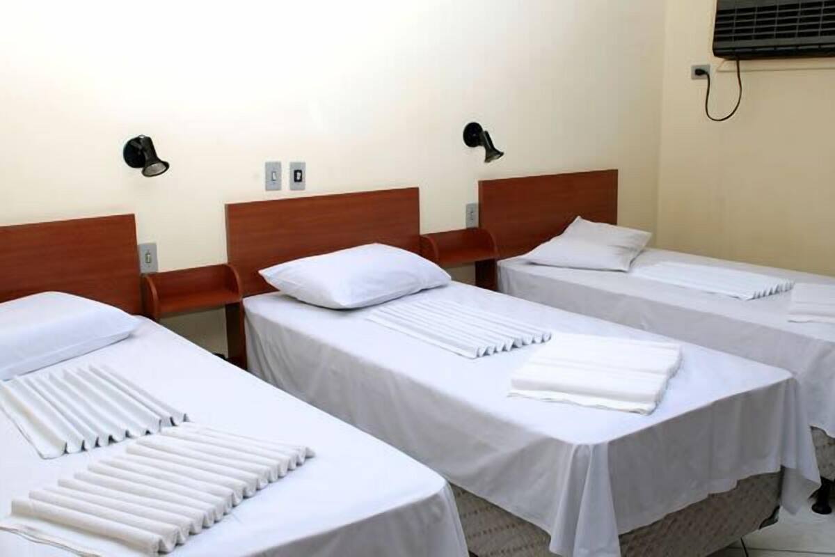 Trois lits simples avec des tĂȘtes de lit en bois, du linge de lit blanc et des lampes de chevet.
