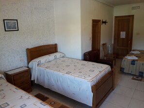 Een slaapkamer met een bed, een houten nachtkastje, een dressoir, een stoel en een tafel met tafelkleed.
