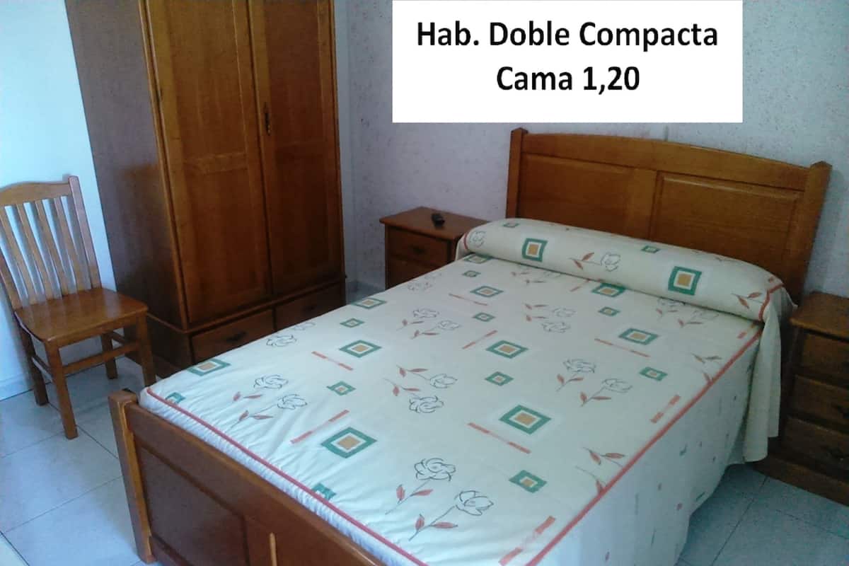 Een compacte tweepersoonskamer met een bed, een houten garderobe en een stoel.