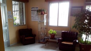 Een kamer met twee leren fauteuils, een glazen vitrinekast, een potplant en een radiator.