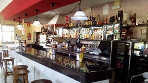 Een bar met een lange toonbank, krukken en schappen vol flessen.