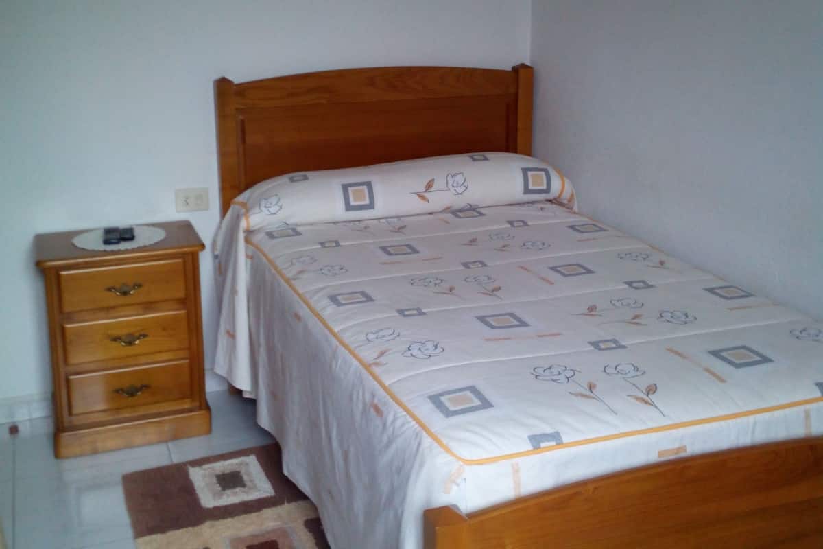 Een kleine, verzorgde slaapkamer met een enkel bed, een houten nachtkastje en een nachttafel.