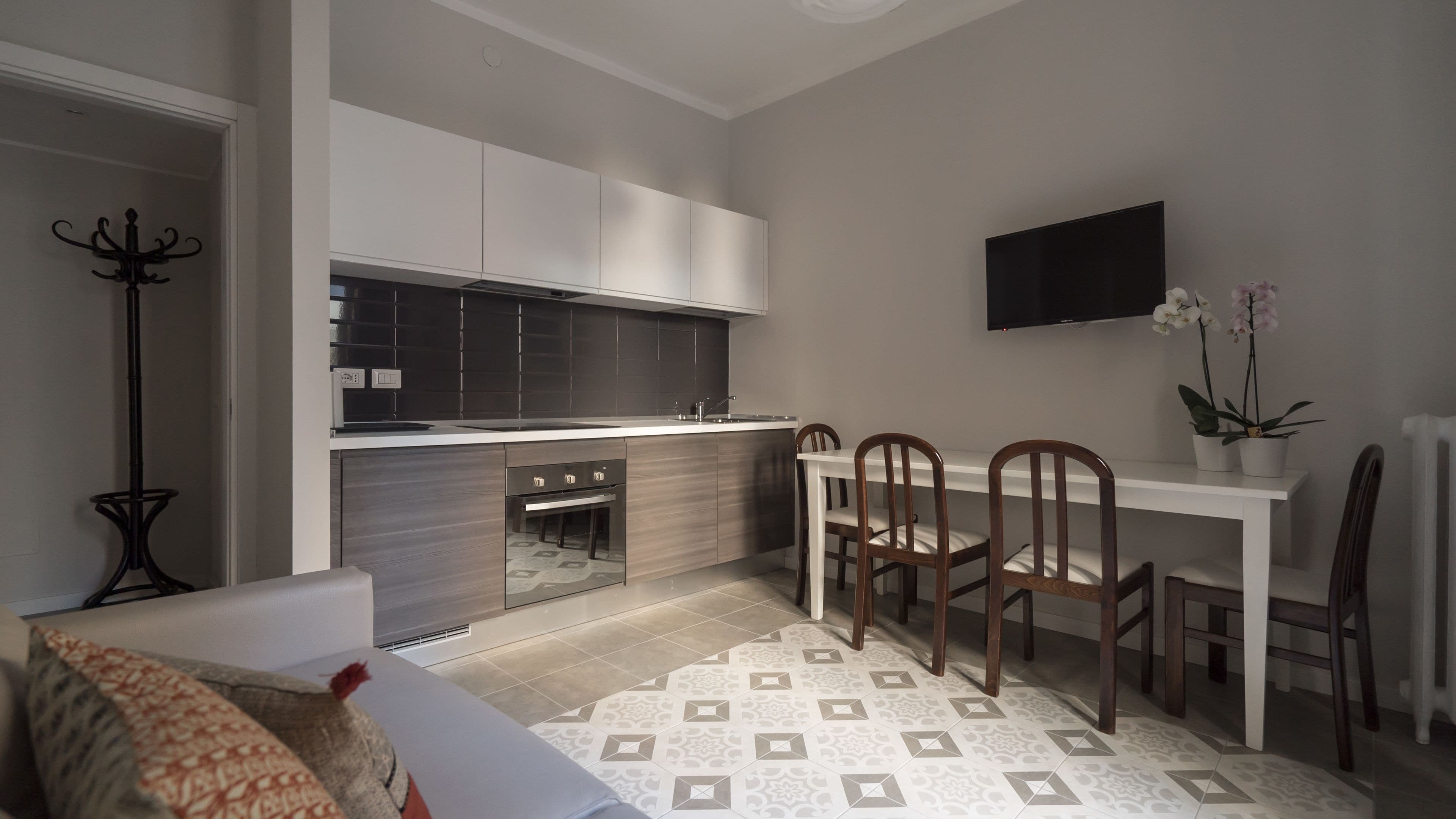 Une cuisine compacte dotée d’appareils électroménagers modernes, un coin repas avec des chaises en bois et un téléviseur à écran plat fixé au mur.