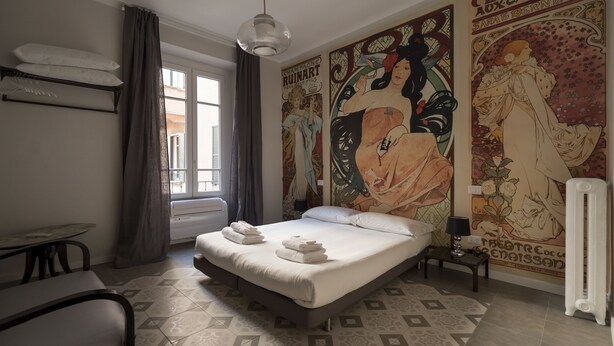 A bedroom with a bed, a radiator, a table, and a window with curtains.