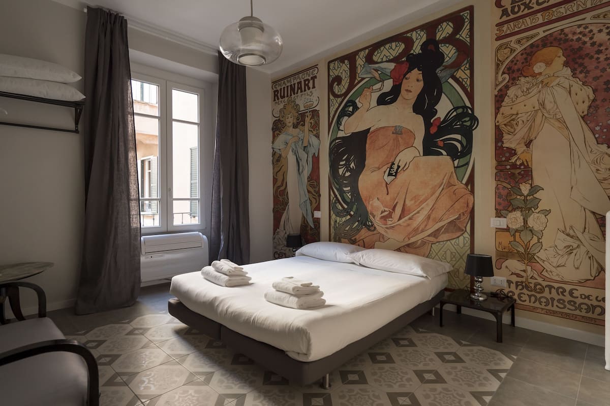 A bedroom with a bed, a radiator, a table, and a window with curtains.
