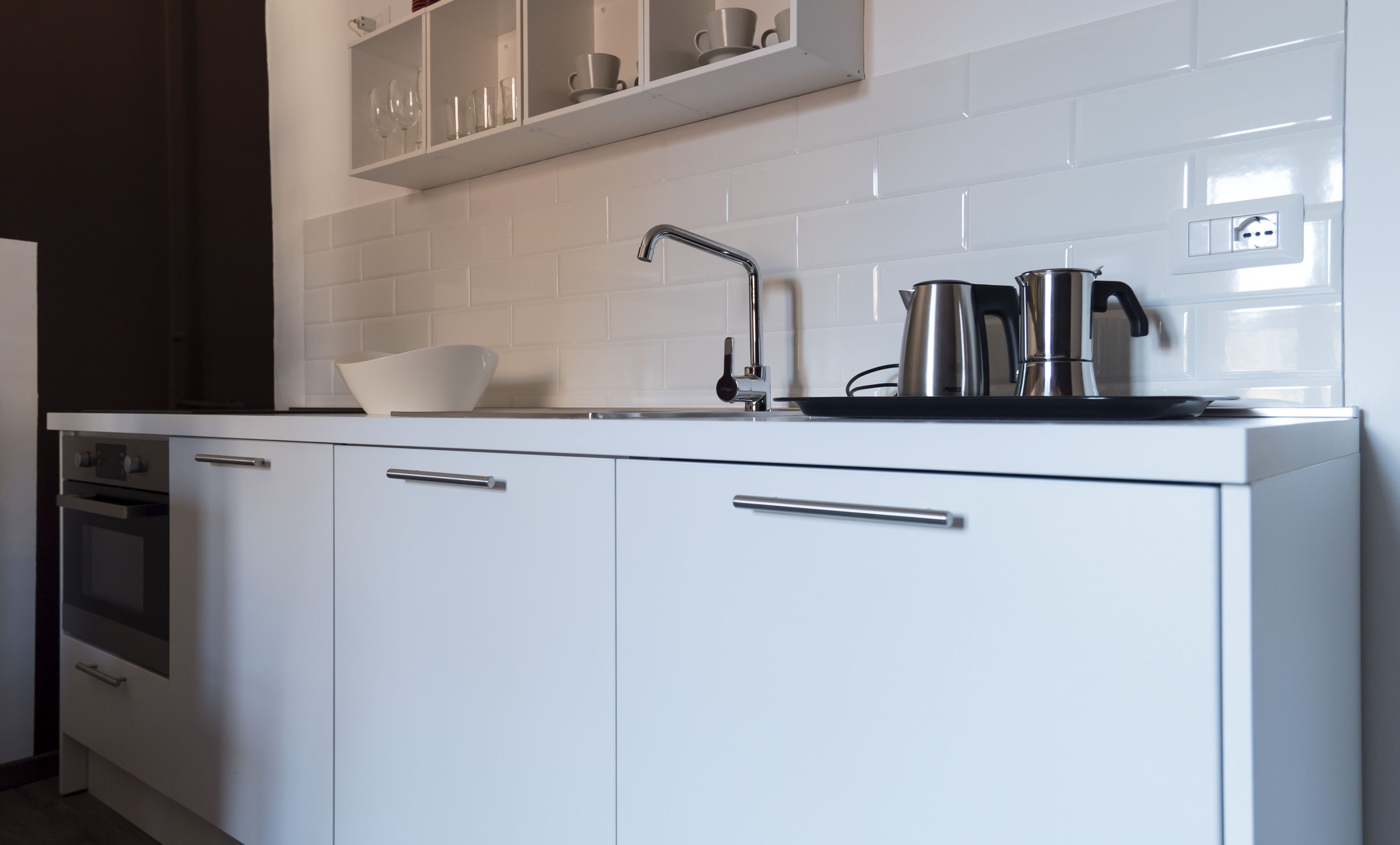A modern kitchen with white cabinets, a stainless steel faucet, and a kettle on the countertop.