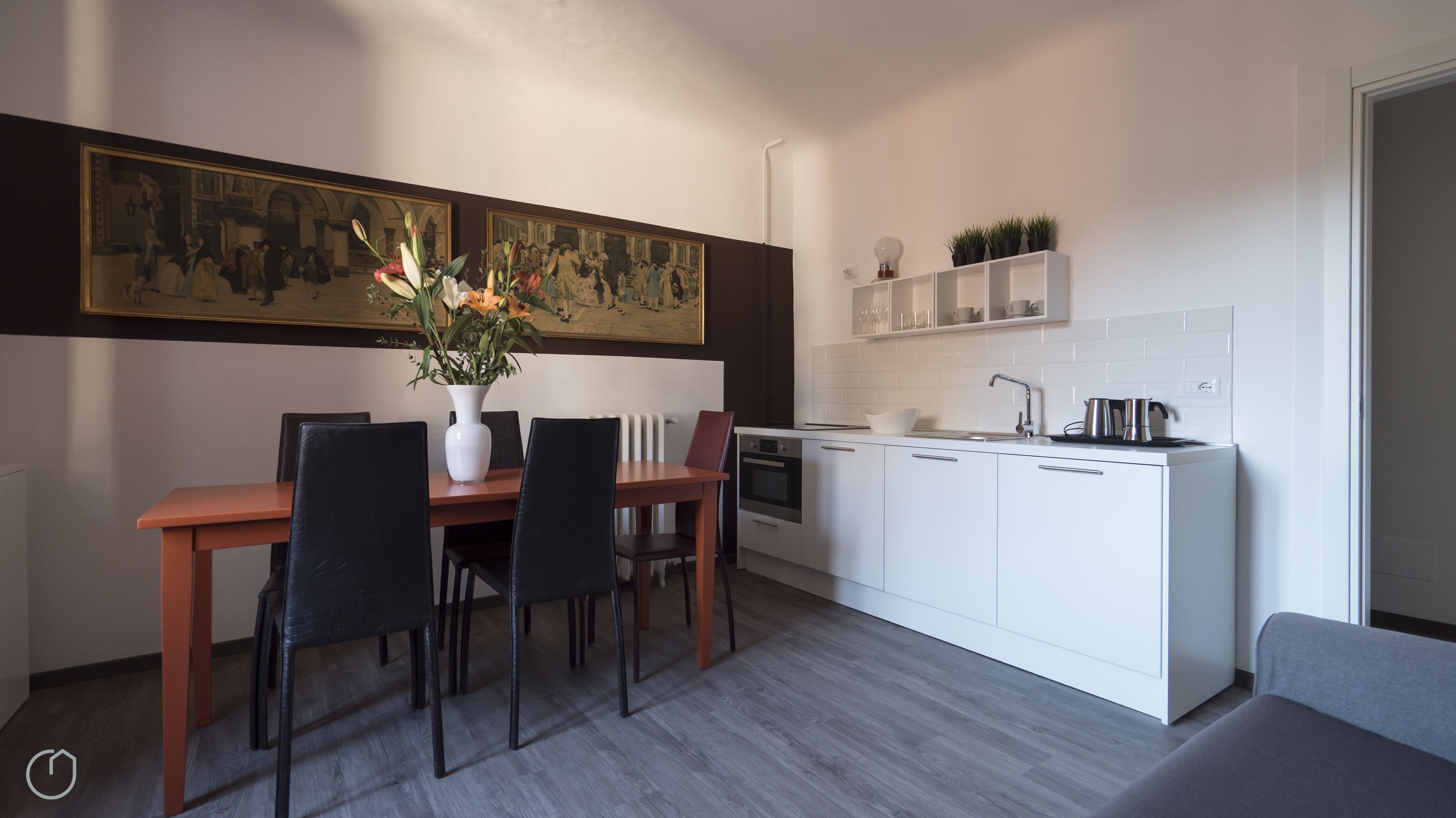 A modern kitchen with white cabinets, a dining table with chairs, a vase of flowers, and a painting on the wall.