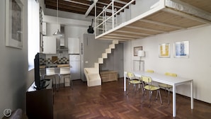 A modern kitchen with white cabinets, a dining area with a white table and yellow chairs, and a staircase leading to an upper level.