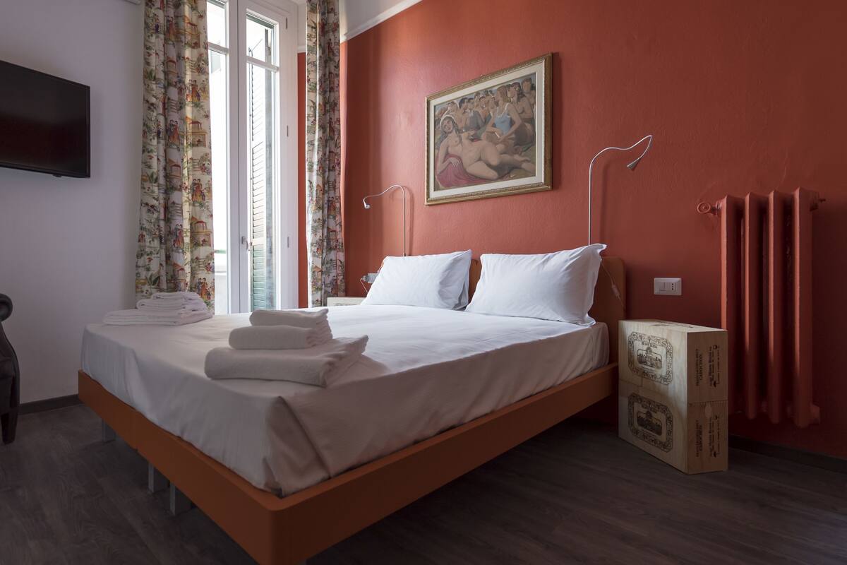 A hotel room with a bed, a flat-screen TV, a painting, and a wooden floor.