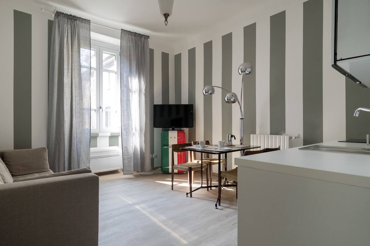 A modern living room with a sofa, a dining table with chairs, a TV, and a kitchen area with a sink and a lamp.