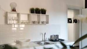 A modern kitchen with white cabinetry, a stainless steel sink, and a countertop with a kettle and a tray.