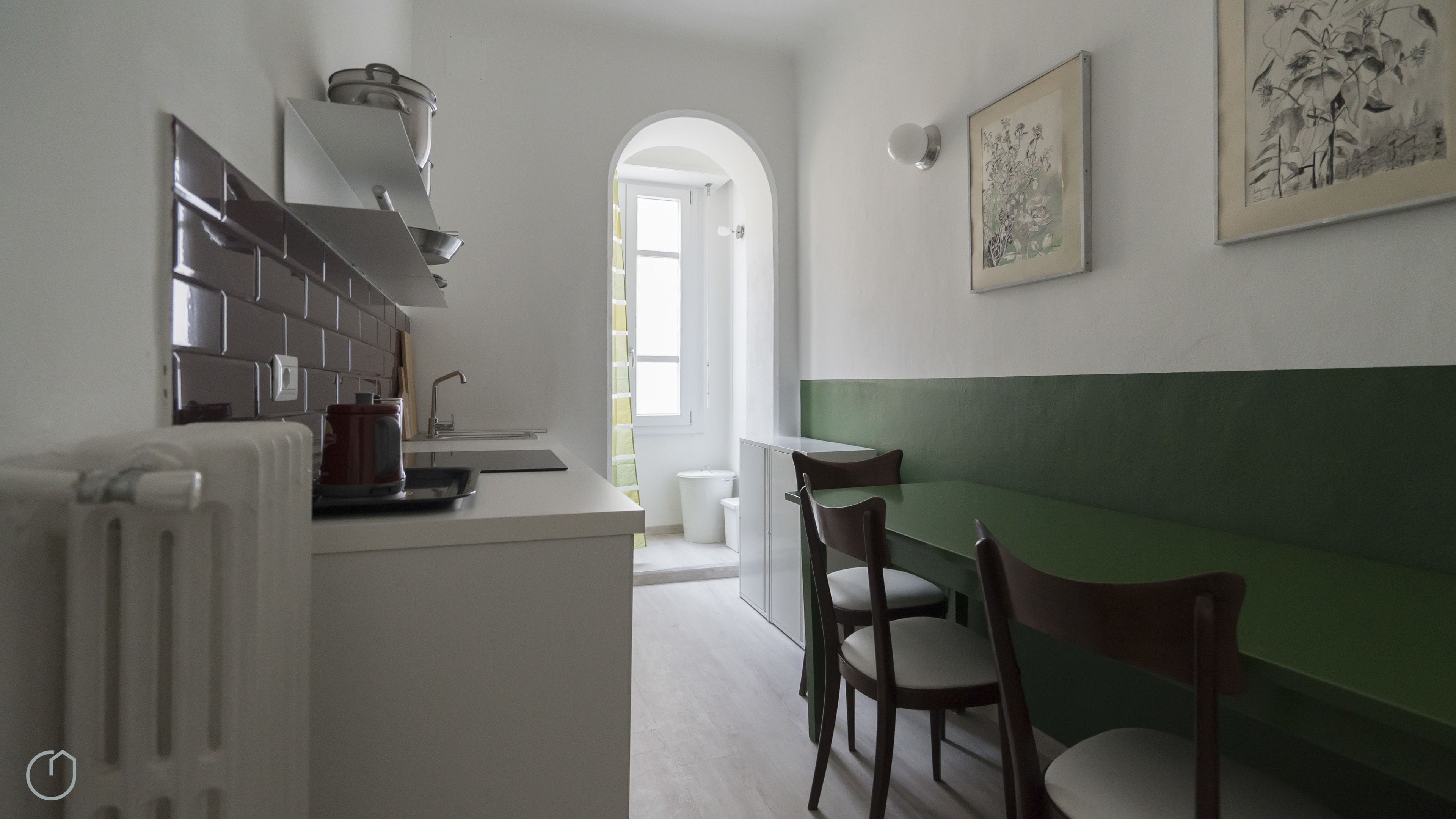 A modern kitchen with a dining area, a radiator, a sink, and a green accent wall.