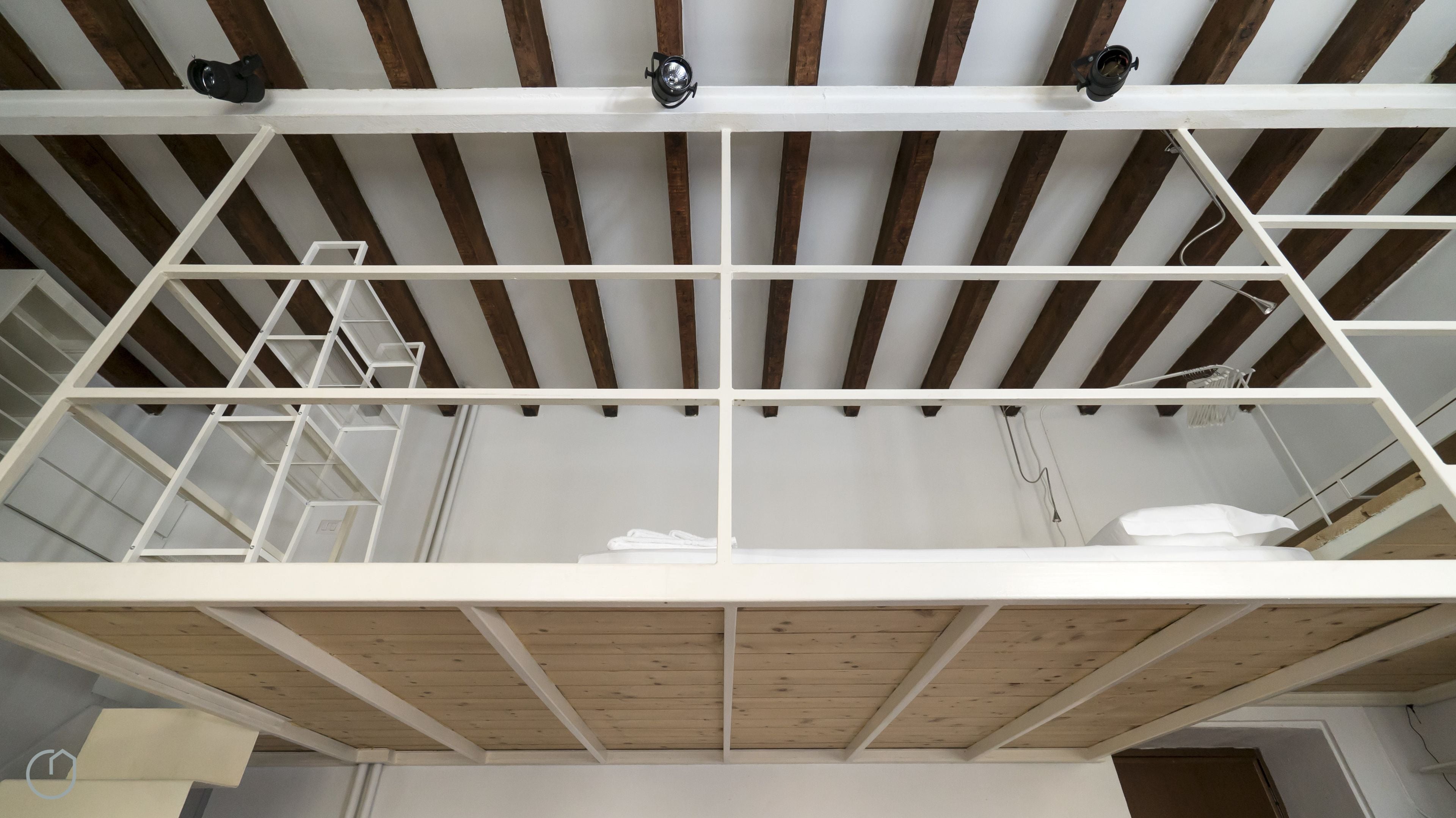 A room with a wooden ceiling, white beams, and a white ladder.