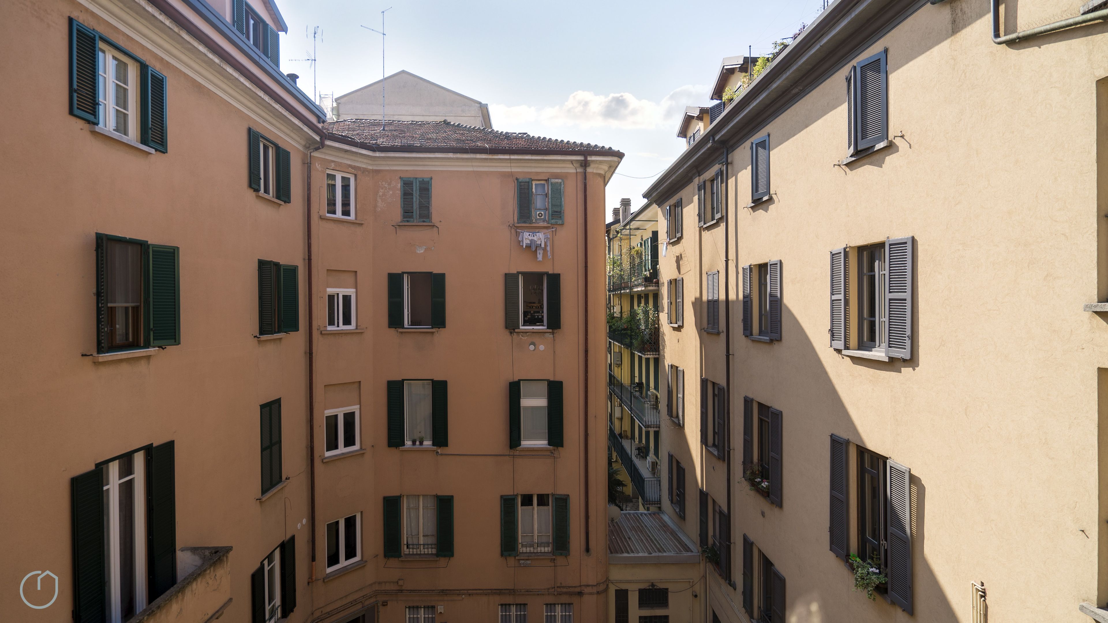 A narrow street between buildings with multiple windows, some with shutters, and balconies.
