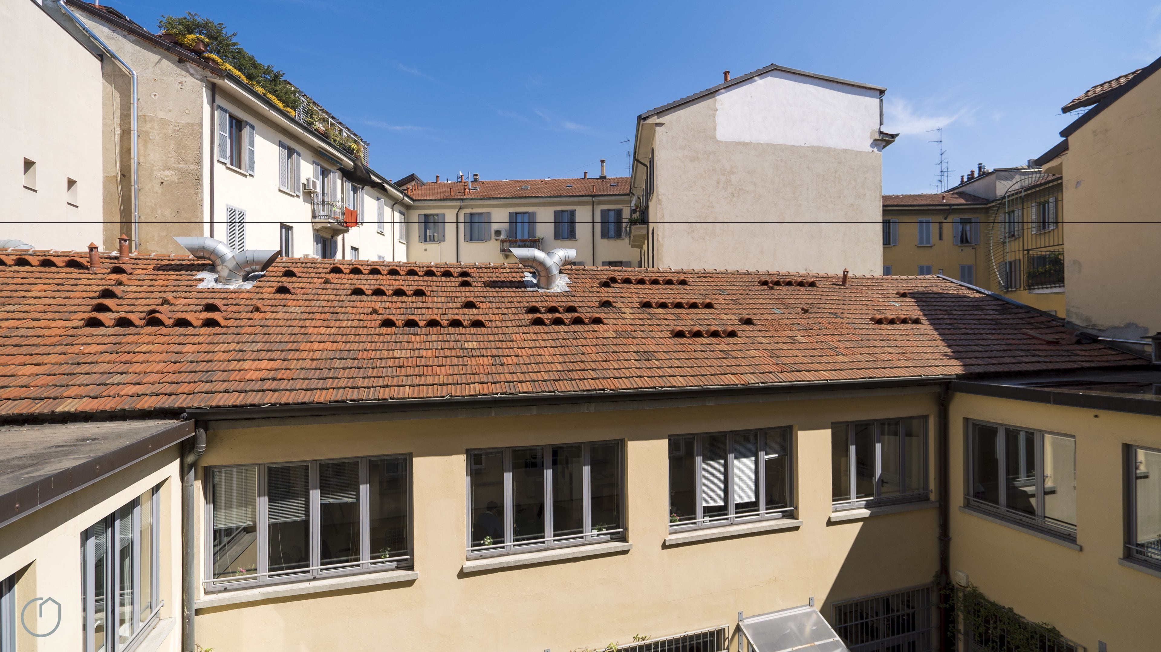 Un bâtiment doté d’un toit recouvert de tuiles, de nombreuses fenêtres et d’une façade plane.