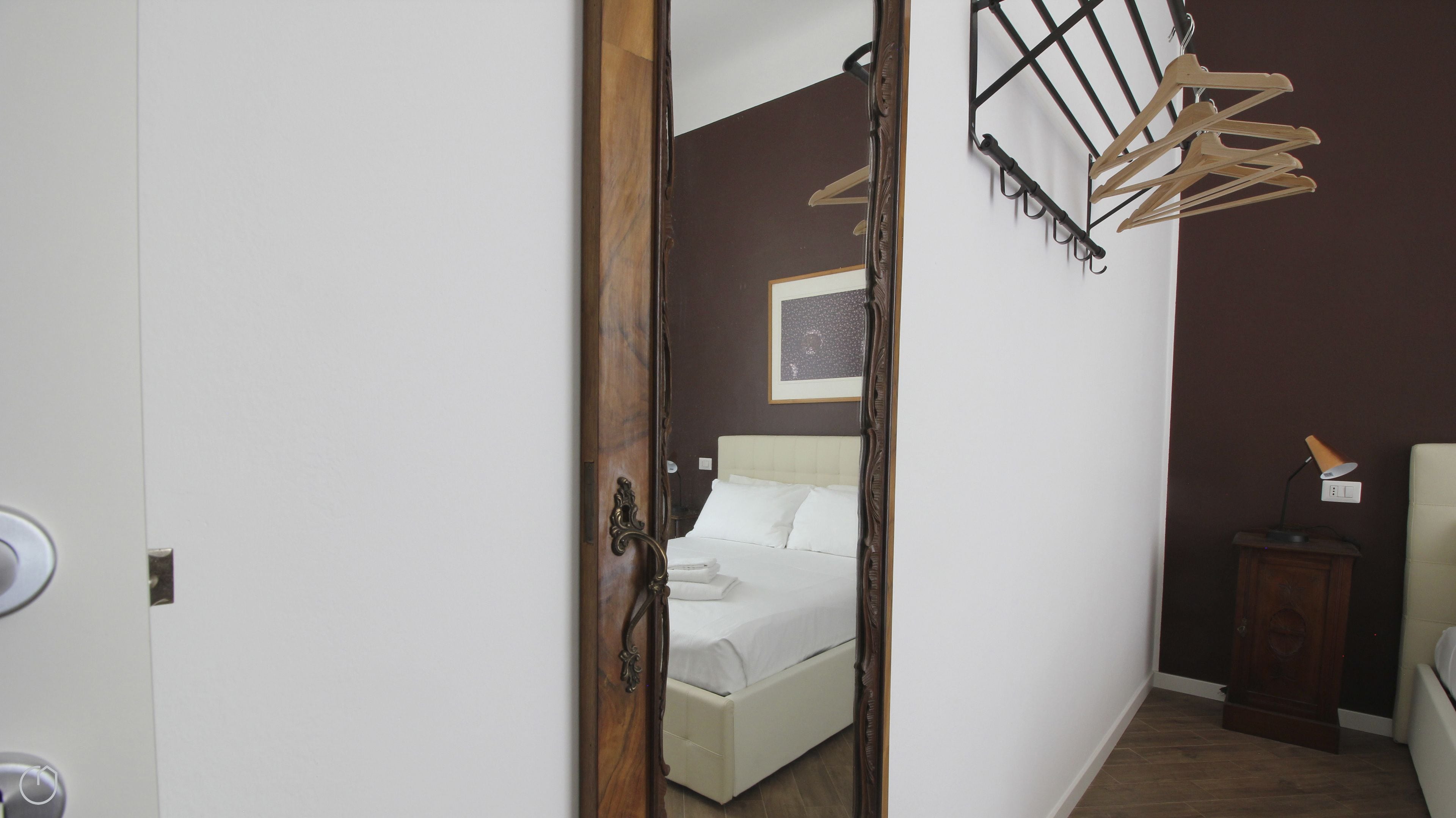 Quarto com cama, porta de madeira, varal fixado na parede e mesa de cabeceira com abajur.