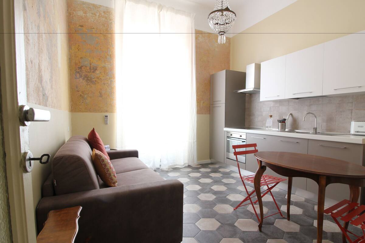 A compact living space with a sofa, a dining table with chairs, a kitchen area with cabinets and a sink, and a patterned floor.