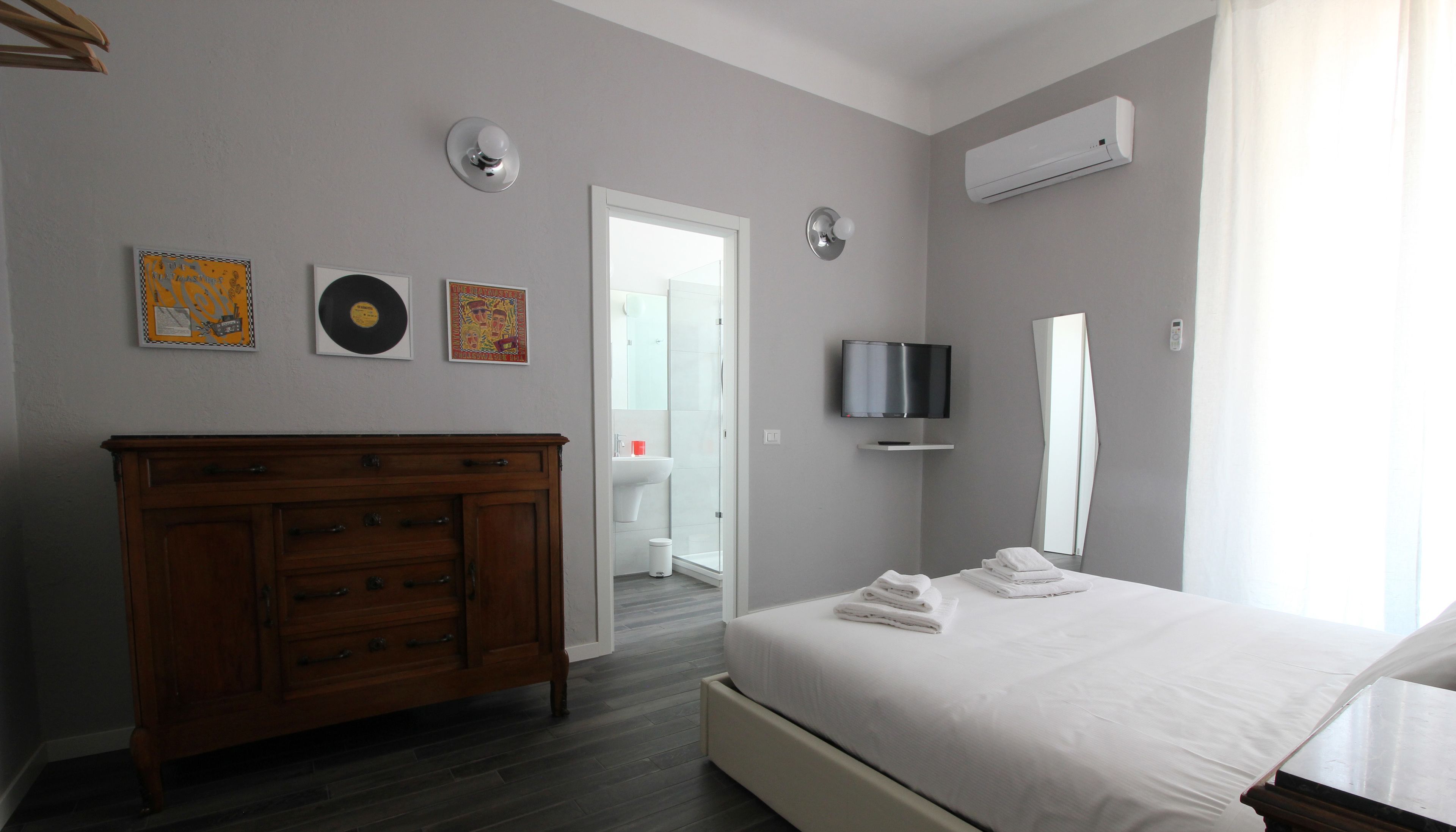 Una habitación de hotel moderna con un aparador de madera, una cama con toallas ordenadas, un televisor de pantalla plana y un espejo grande.