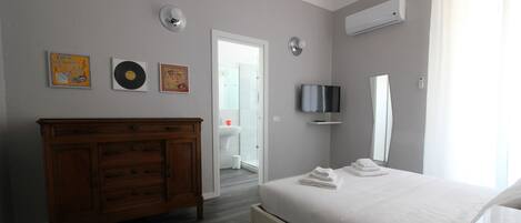Una habitación de hotel moderna con un aparador de madera, una cama con toallas ordenadas, un televisor de pantalla plana y un espejo grande.