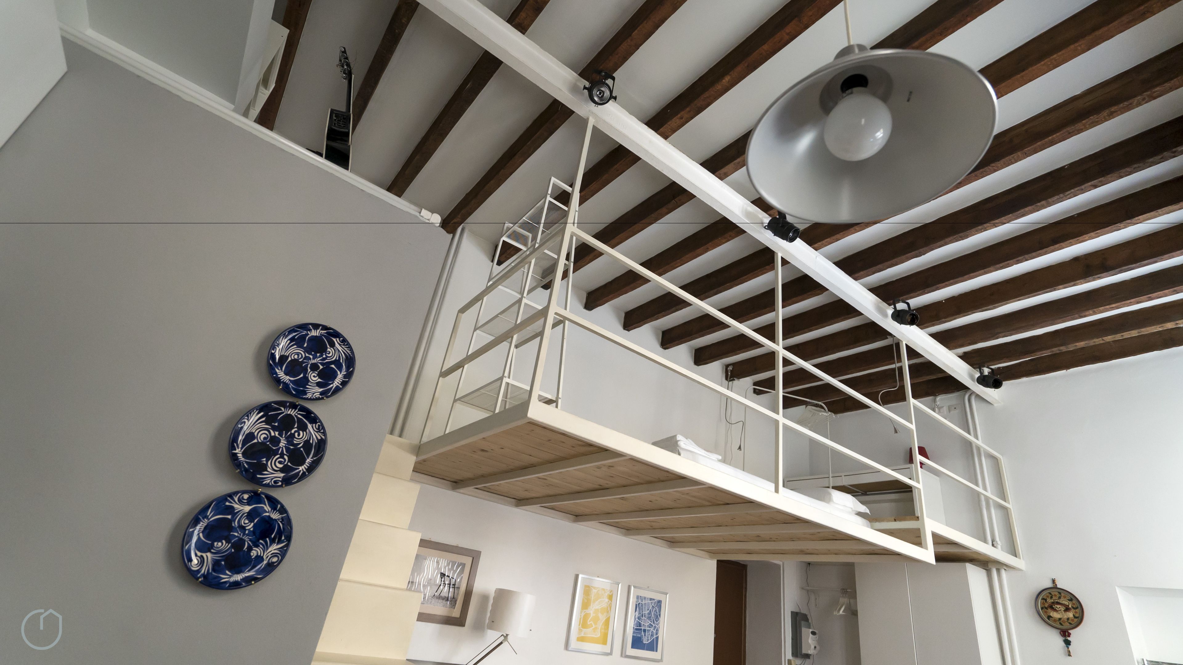A loft-style room with exposed wooden beams, a mezzanine with a white railing, and decorative plates on the wall.