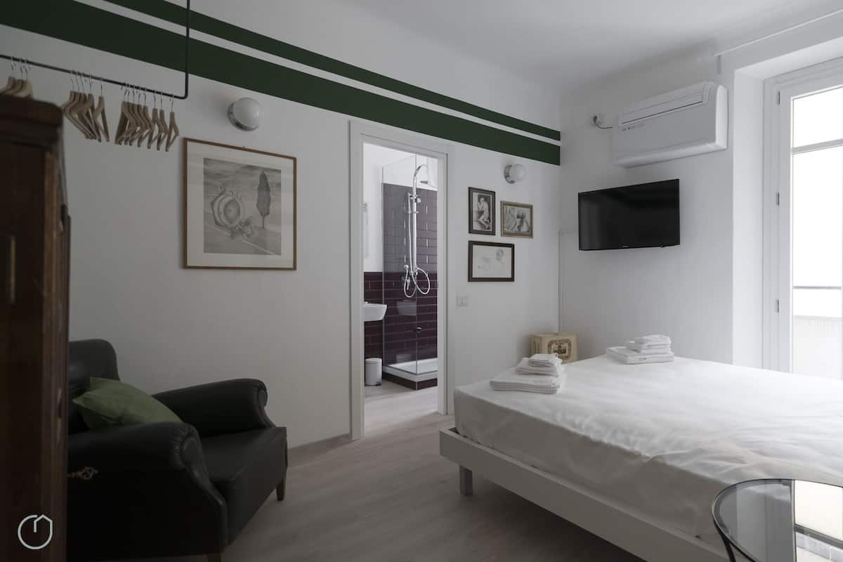 A modern bedroom with a bed, a TV, and a bathroom visible through an open door.