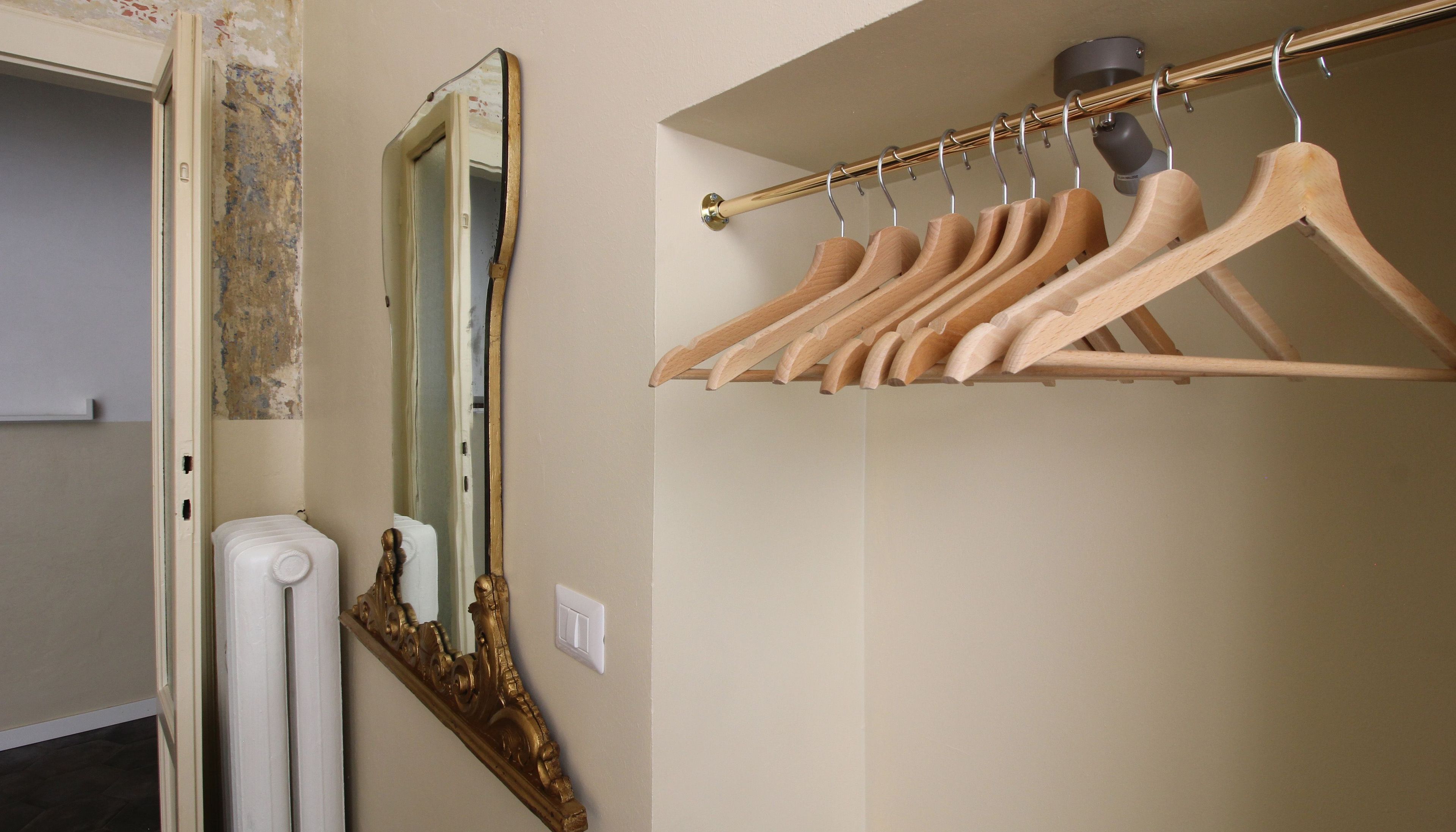 A room with a mirror, a radiator, and a wooden hanger rack with hangers.