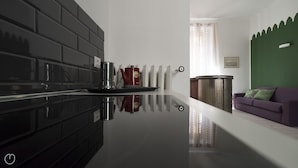 A modern kitchen with a black backsplash, a stainless steel coffee maker, and a reflective countertop.