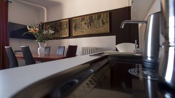 A modern kitchen with a dining area, a coffee machine, and a painting on the wall.