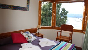 A bedroom with a bed, pillows, a chair, a window, and a view of trees and mountains. - Don Justo (San Carlos de Bariloche)