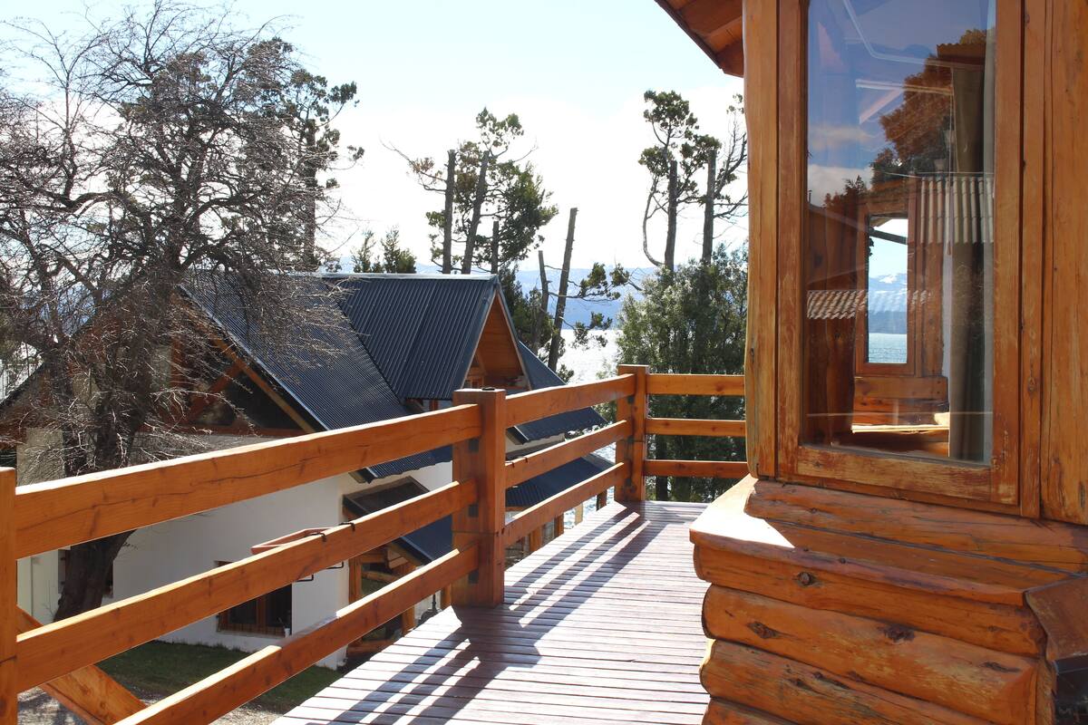 Une terrasse en bois dotée d’une rambarde, offrant une vue sur un paysage montagneux et une étendue d’eau.