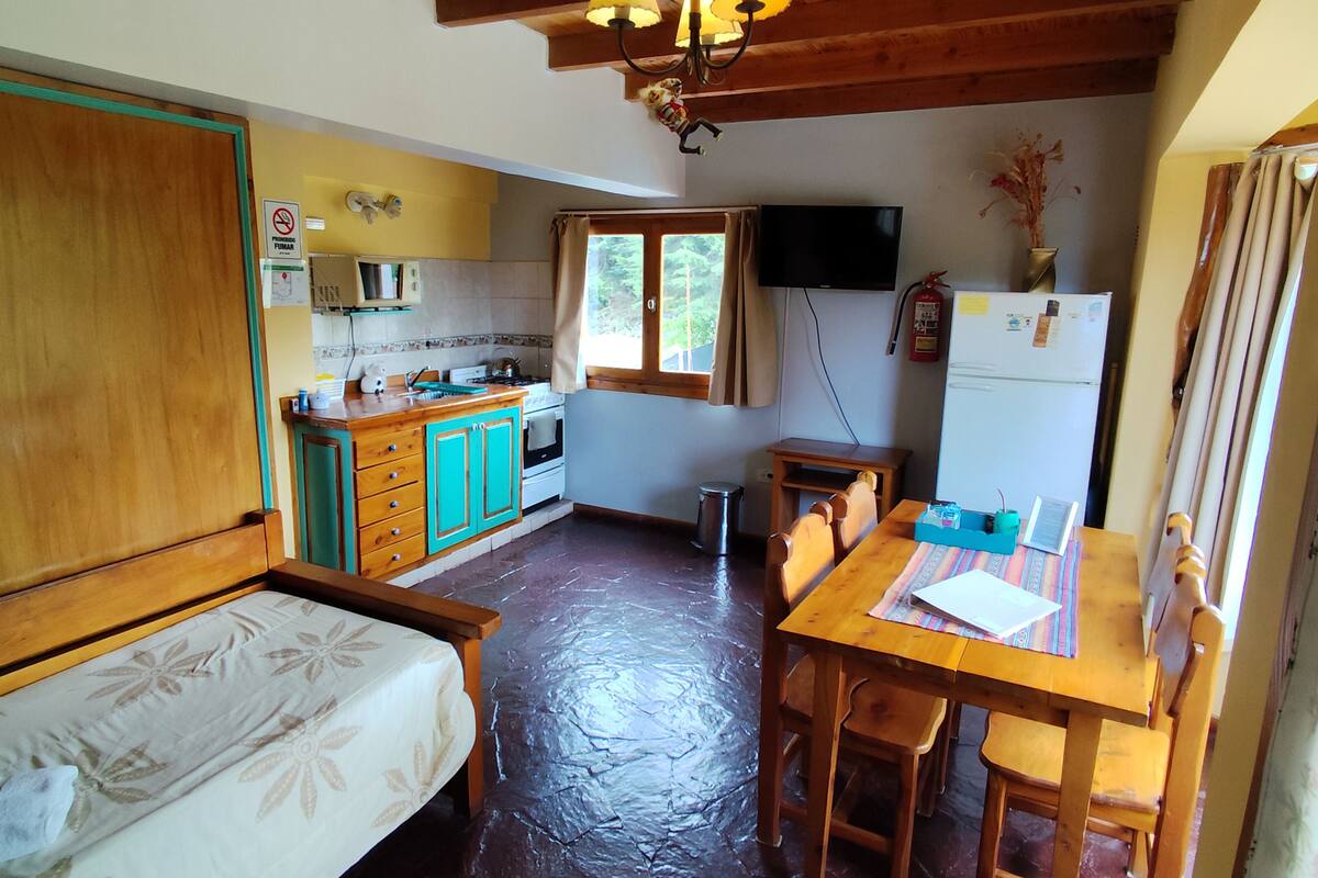 Une cuisine compacte avec un coin repas, des meubles en bois et un téléviseur fixé au mur.