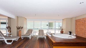 A modern indoor pool area with lounge chairs, a hot tub, and a view of the outside. - Beach Class - MeuLugarCeará (Fortaleza)