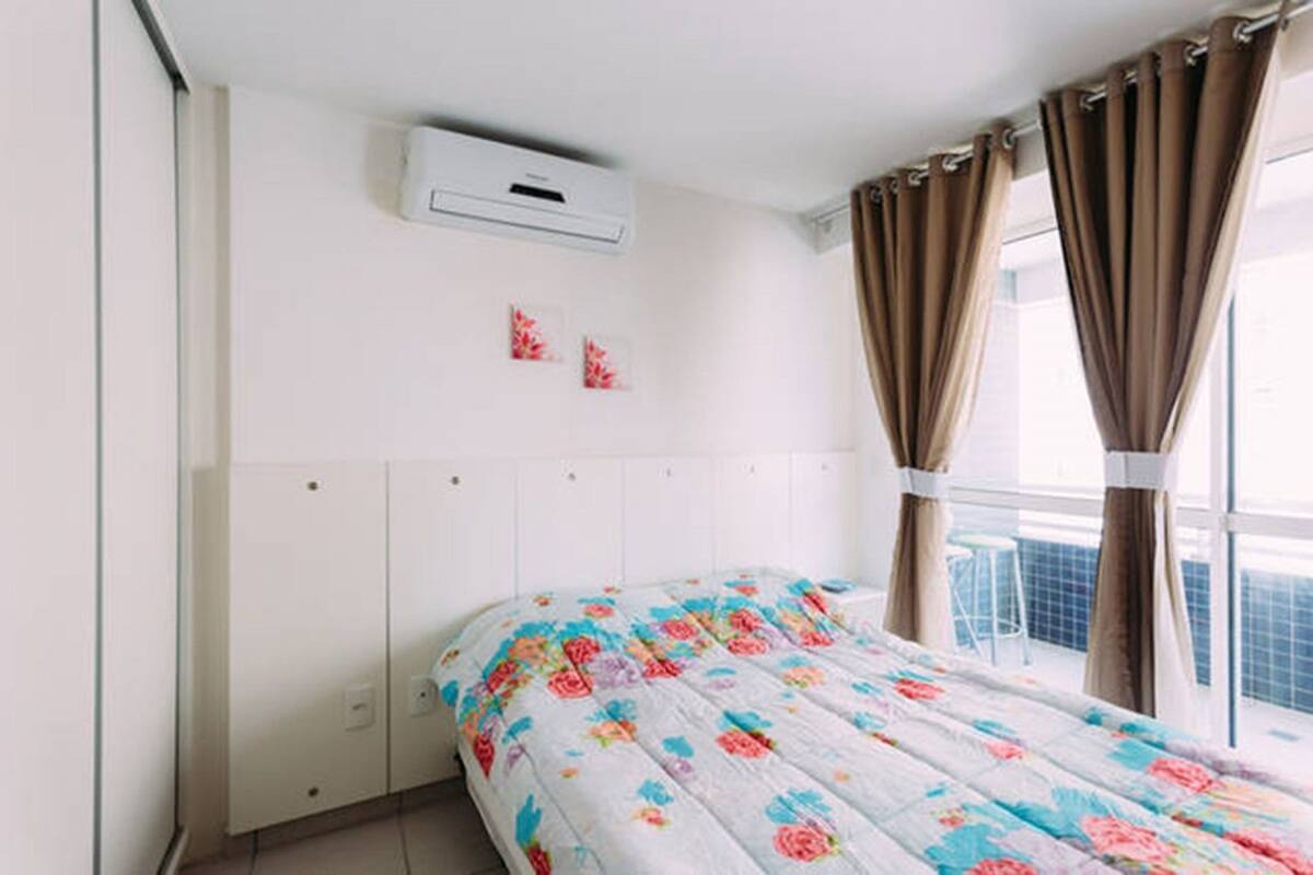 Ein Schlafzimmer mit Bett, weißem Kopfteil, Klimaanlage und Vorhängen.