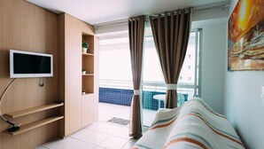 A hotel room with a bed, a TV mounted on the wall, a small shelf with a plant, and a view of the outside balcony. - Beach Class - MeuLugarCeará (Fortaleza)