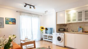 A modern kitchen with a washing machine, a dining area with a table set for breakfast, and a large window with curtains.